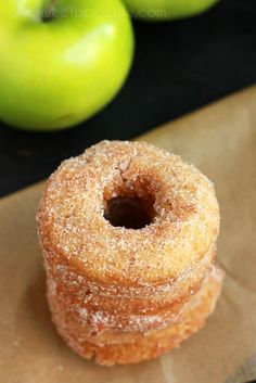 three donuts sitting on top of brown paper next to green apples