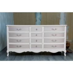 a white dresser with many drawers in the middle and blue paint on the wall behind it