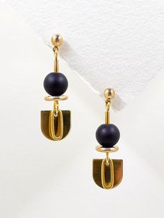 These earrings are sleek and modern, crafted from golden brass and semi precious stone.  The matte, black onyx stone features among the geometric shapes, an elongated semi-circle, layered with a solid brass oval hangs below, adding a touch of contrast and sophistication to the overall design.  The combination of geometric shapes, the matte black stone, and the metallic shine creates an elegant, minimalist aesthetic. A brass ball stud with stainless steel post holds the design from the top.  Approximate measurements- 4.5cms long 1.5cms wide All Set Theory jewellery comes with care instructions and a polishing pad to keep your jewellery looking shiny and fabulous! ✨ Modern Gold Onyx Earrings, Modern Black Geometric Earrings, Minimalist Black Brass Jewelry, Set Theory, Black Statement Earrings, Dangle Earrings Gold, Gold Dangle Earrings, Stone Feature, Black Onyx Stone