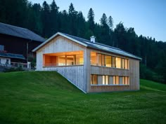 a wooden house sitting on top of a lush green hillside next to a forest at night