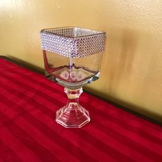 a glass candle holder sitting on top of a red table cloth