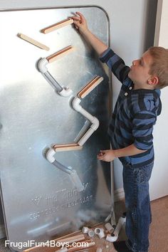 a little boy that is standing in front of a metal wall with pipes on it