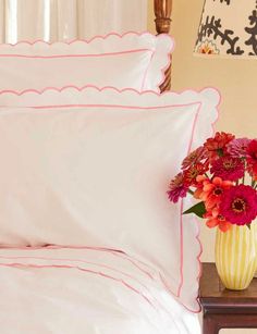 a vase filled with red flowers sitting on top of a table next to a bed