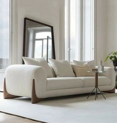 a living room with a white couch, mirror and potted plant in the corner