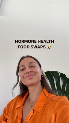 a woman in an orange shirt smiles at the camera while standing next to a plant