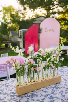 flowers are arranged in vases on top of a wooden stand at an outdoor party