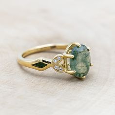 a ring with a green stone and diamonds on the side, sitting on a wooden surface