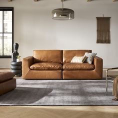 a brown leather couch sitting on top of a rug in a living room next to a window