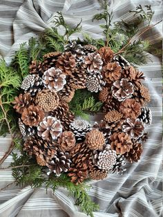 a wreath made out of pine cones and evergreen needles on a gray striped cloth with green branches