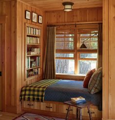 a bedroom with wood paneling and a bed in front of a window filled with books