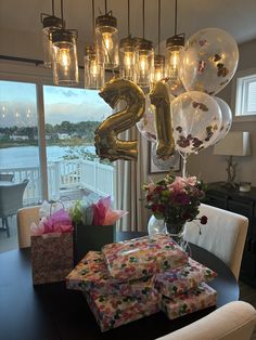 balloons and presents on a table in front of a window with the number 25 hanging from it