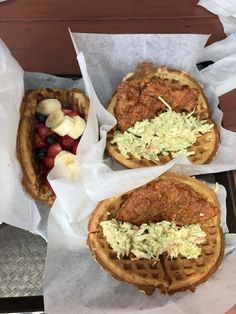 two waffles with chicken and cole slaw on them sitting in paper wrappers