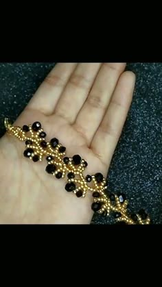 a hand holding a gold bracelet with black beads