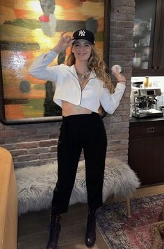 a woman standing in front of a brick wall wearing black pants and a white shirt