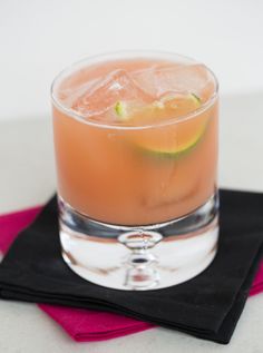 a glass filled with a drink sitting on top of a black cloth next to a pink napkin