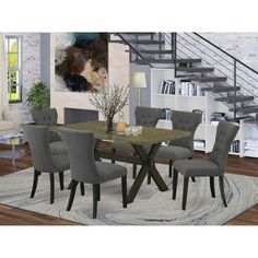 a dining room table with grey chairs in front of a stair case and bookshelf