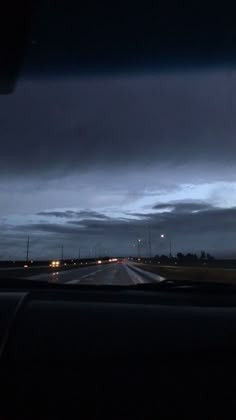 the night sky is dark and cloudy as seen from inside a moving car on an empty highway