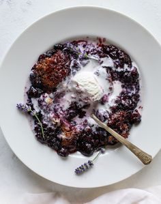 a white plate topped with blueberry cobble next to a spoon and ice cream