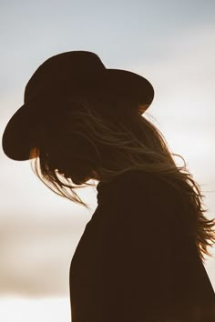 the silhouette of a person wearing a hat with long hair in front of a cloudy sky