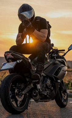 a man riding on the back of a motorcycle in front of an orange sky at sunset