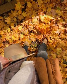 a person laying on the ground with their feet up and wearing a hat in front of autumn leaves