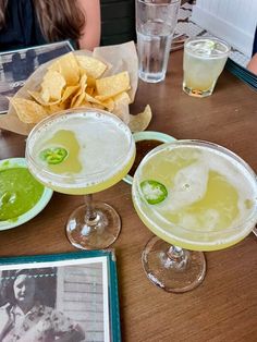 two margaritas are sitting on a table with chips