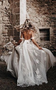 a woman in a wedding dress sitting on the ground with her back to the camera