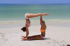 two women in bikinis doing yoga on the beach