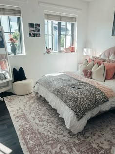 a bedroom with a large bed and two windows in the corner, along with an area rug on the floor