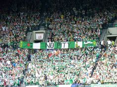 a large group of people sitting in the stands at a soccer game, with one person holding up a green and white banner