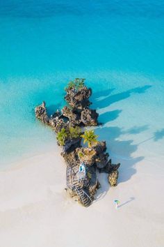 an aerial view of a beach with rocks and palm trees in the sand, blue water and white sand