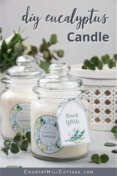 two jars filled with white candles sitting on top of a table next to green leaves