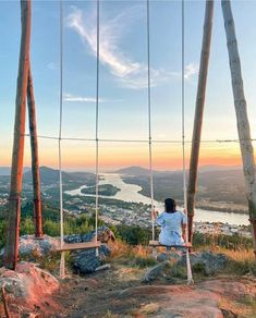 a woman is sitting on a swing overlooking the water