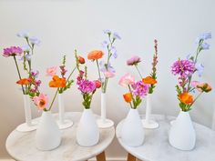 four white vases filled with different colored flowers on top of a marble topped table