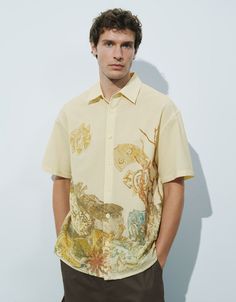 a man standing in front of a white wall wearing a shirt with animals on it