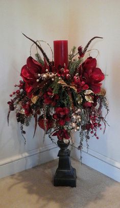 a vase with red flowers and greenery in it next to a lit candle on the floor