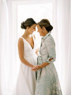 two women standing next to each other in front of a window