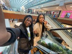 two people standing on an escalator in a shopping mall posing for the camera