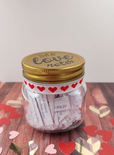 a jar filled with lots of love notes on top of a wooden table next to confetti