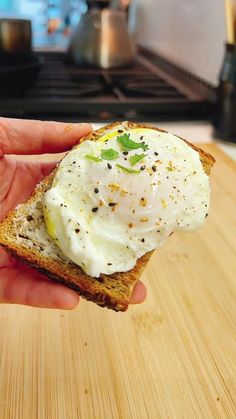 a person holding up a piece of bread with an egg on it and sprinkled with parsley