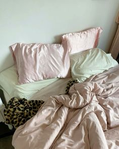 an unmade bed with pink comforter and leopard print pillows on top of it