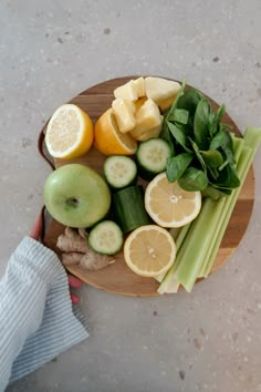 a wooden plate topped with sliced up fruit and veggies next to a person's hand