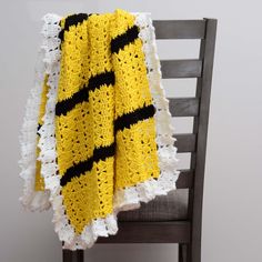 a yellow and black crocheted blanket sitting on top of a wooden chair