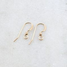 two pairs of gold earrings sitting on top of a white surface with one earring in the shape of an o - ring