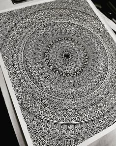 an intricate black and white drawing is on the table next to some pens, pencils and paper