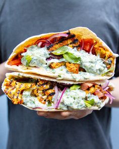 a person holding two tacos filled with different types of vegetables and sauce on them