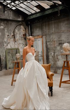 a woman in a white wedding dress standing next to an orange chair and wooden table