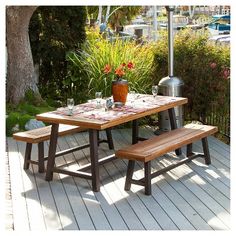 a picnic table with an umbrella over it on a deck next to flowers and trees