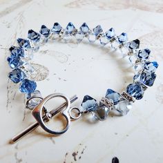 Elegant light blue sapphire and denim blue crystal bracelet is a great gift for women who love exquisite and sparkly blue jewelry. Handmade with Swarovski crystals and Swarovski rhinestone crowns and finished with a sterling silver toggle clasp.  A great gift for a mother of the bride or groom's mom. Luxe and gorgeous sapphire anniversary gift for your wife. A thoughtful gift for a woman born in September since blue sapphire is her birthstone. Bracelet Details: - Bracelet is .5 inches wide (1.27 Blue Crystal Bracelets For Anniversary, Adjustable Blue Crystal Bracelet For Anniversary, Blue Crystal Bracelet With Sparkling Stones, Elegant Blue Faceted Crystal Bracelet, Blue Faceted Crystal Bracelets, Handmade Blue Crystal Bracelet, Blue Faceted Crystal Bracelet For Gifts, Blue Faceted Crystal Bracelet Gift, Blue Crystal Bracelet