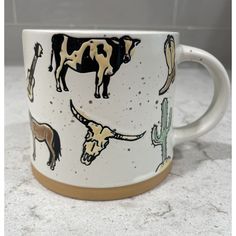 a coffee mug with an image of cows and cactuses painted on it's side